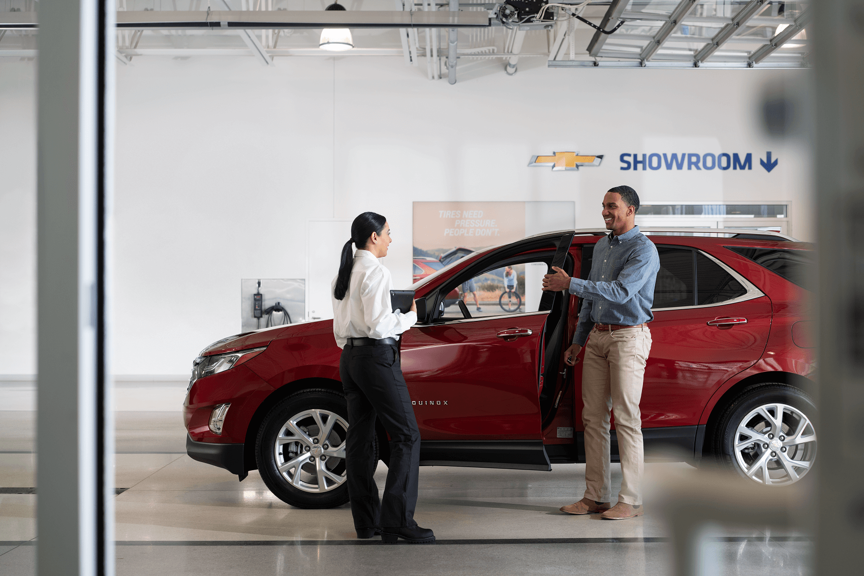 smiling sales professional helps happy customer into new red chevy equinox