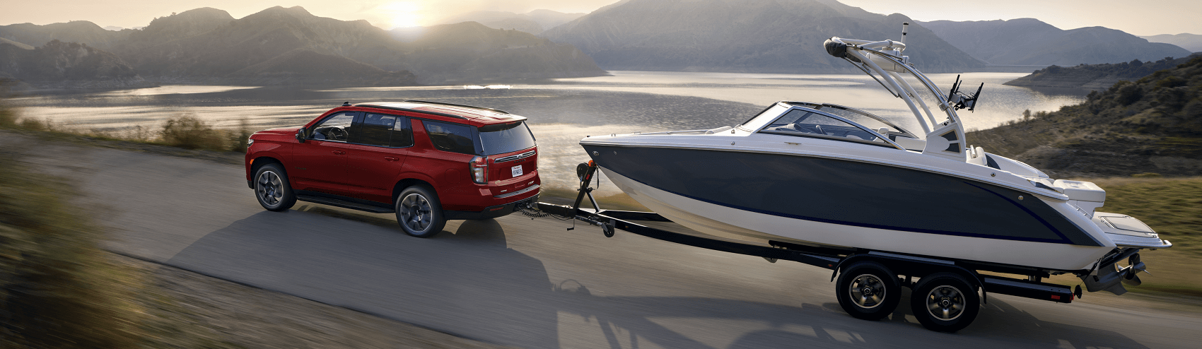 red chevy SUV towing boat along lakeside river