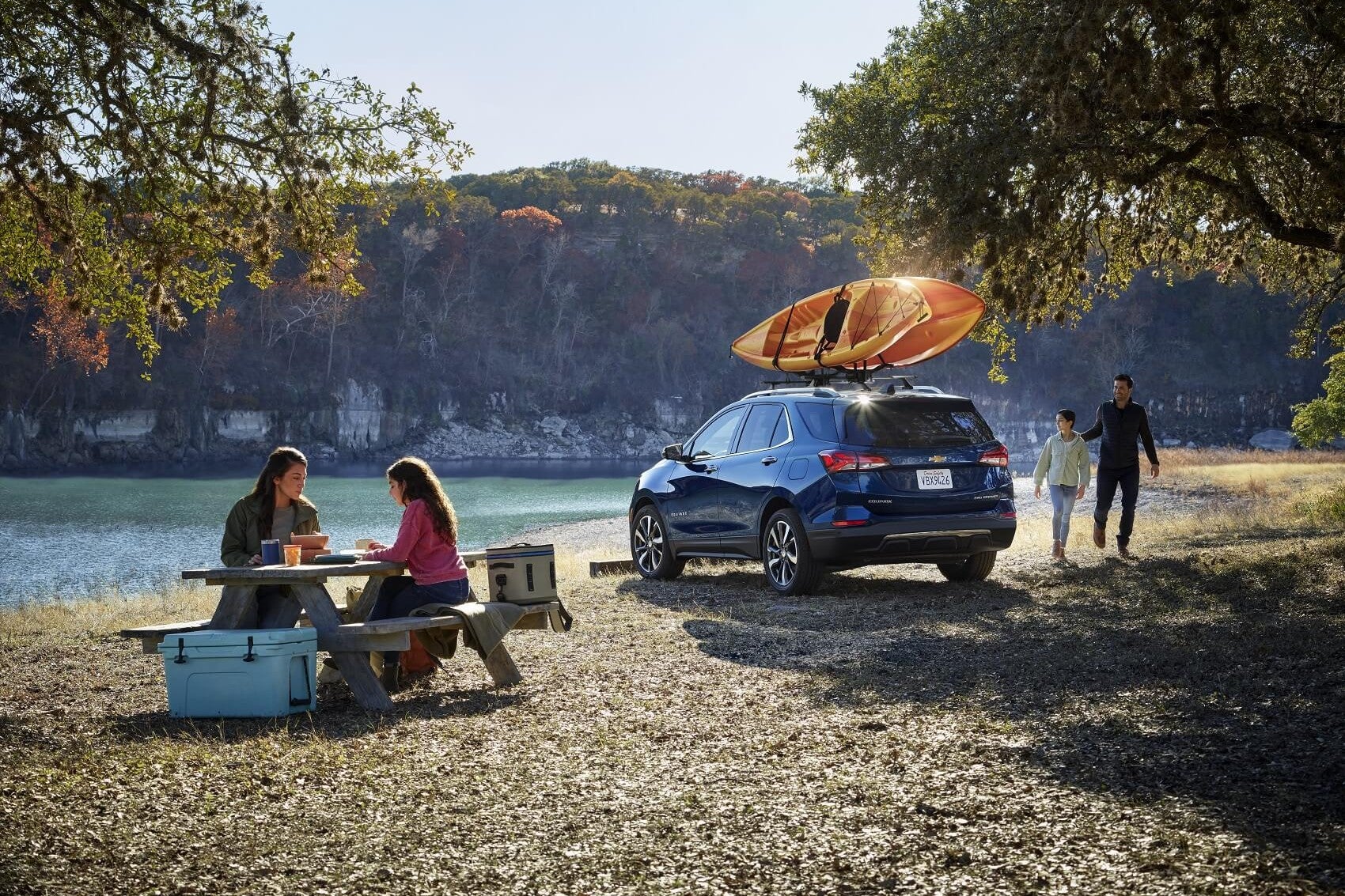blue chevy blazer parked at a campsite with kayak on top and family camping beside a lake